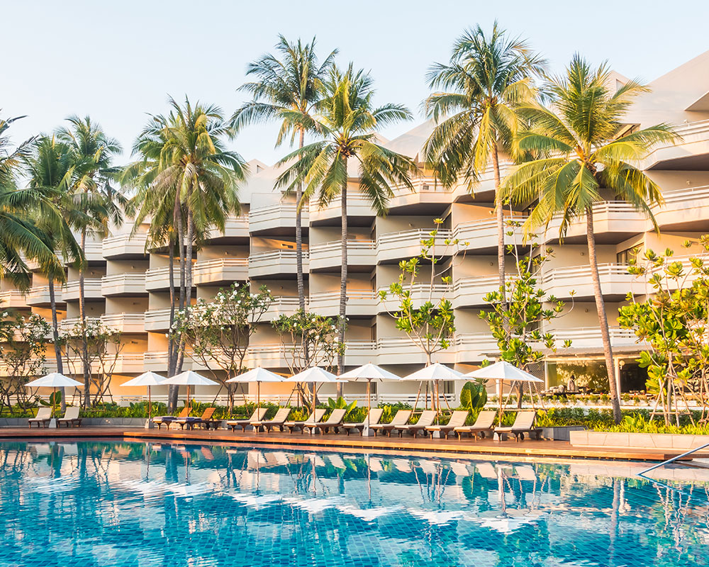 A resort-style swimming pool surrounded by palm trees, representing the accommodation for Baudin Beach Apartment 2.
